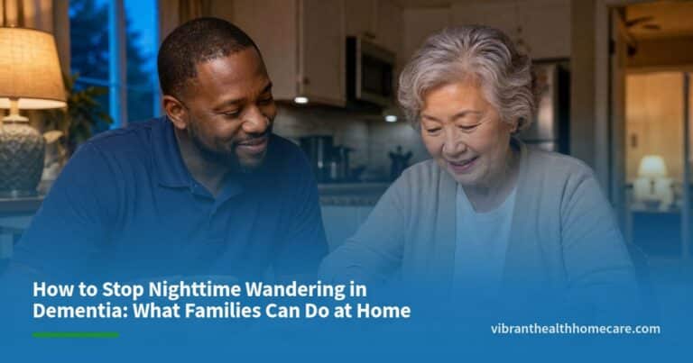 A caregiver and an older woman share tea and look through a photo album at a kitchen table in warm evening light.